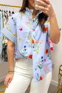 Person wearing a colorful floral shirt taking a mirror selfie in a clothing store.