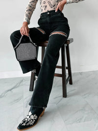 Person wearing black jeans and floral shoes, holding a textured handbag on a white marble floor.