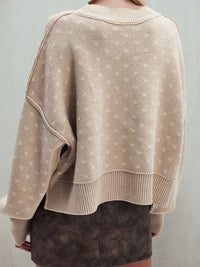 Beige knitted sweater worn by a person on a plain background