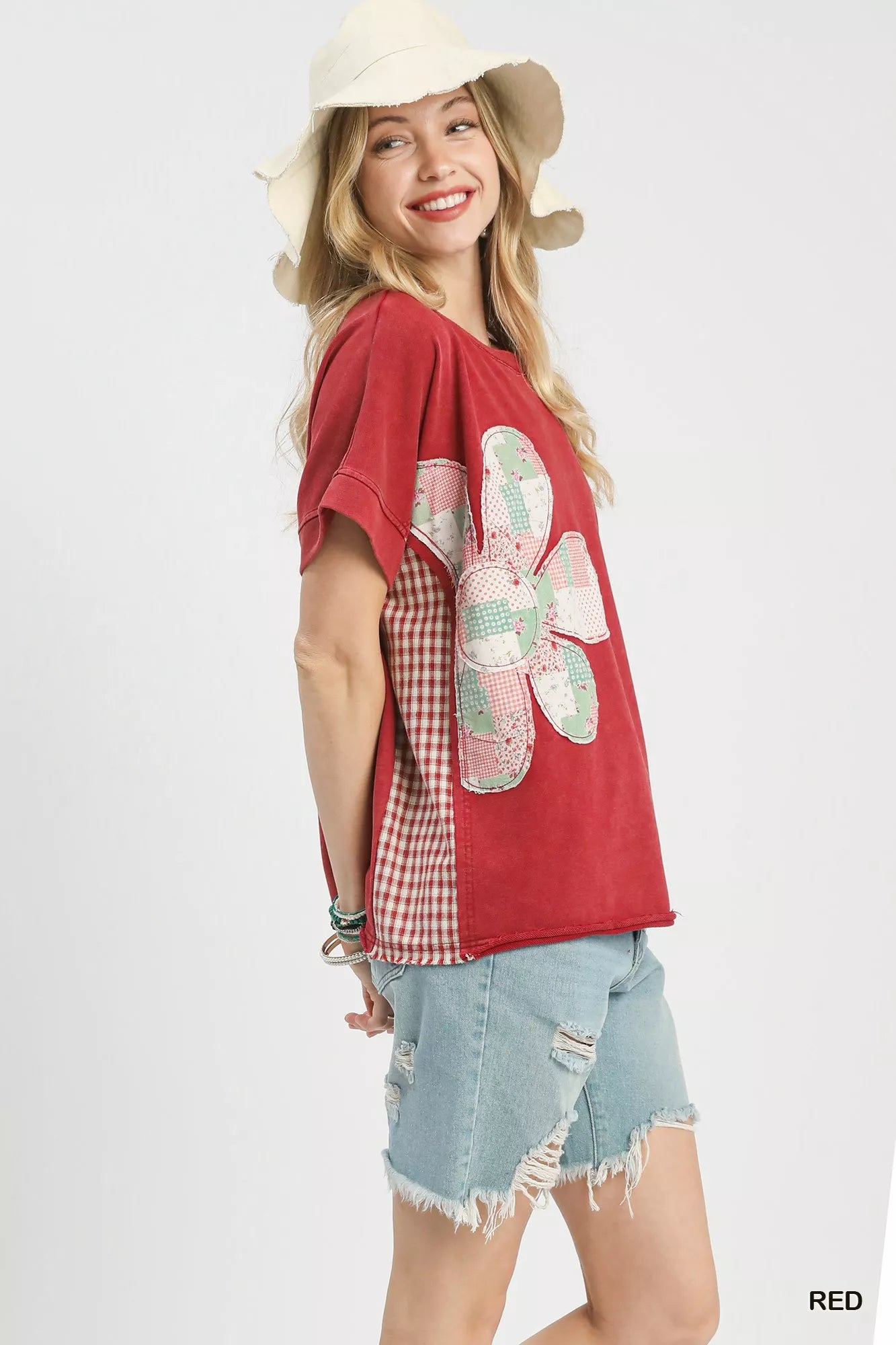 Woman wearing a red shirt with a floral design and denim shorts on a white background