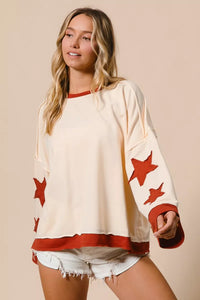 Woman wearing a cream sweater with red star patterns and denim shorts on a beige background