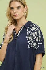 Woman wearing a navy blue blouse with white embroidery on a light green background