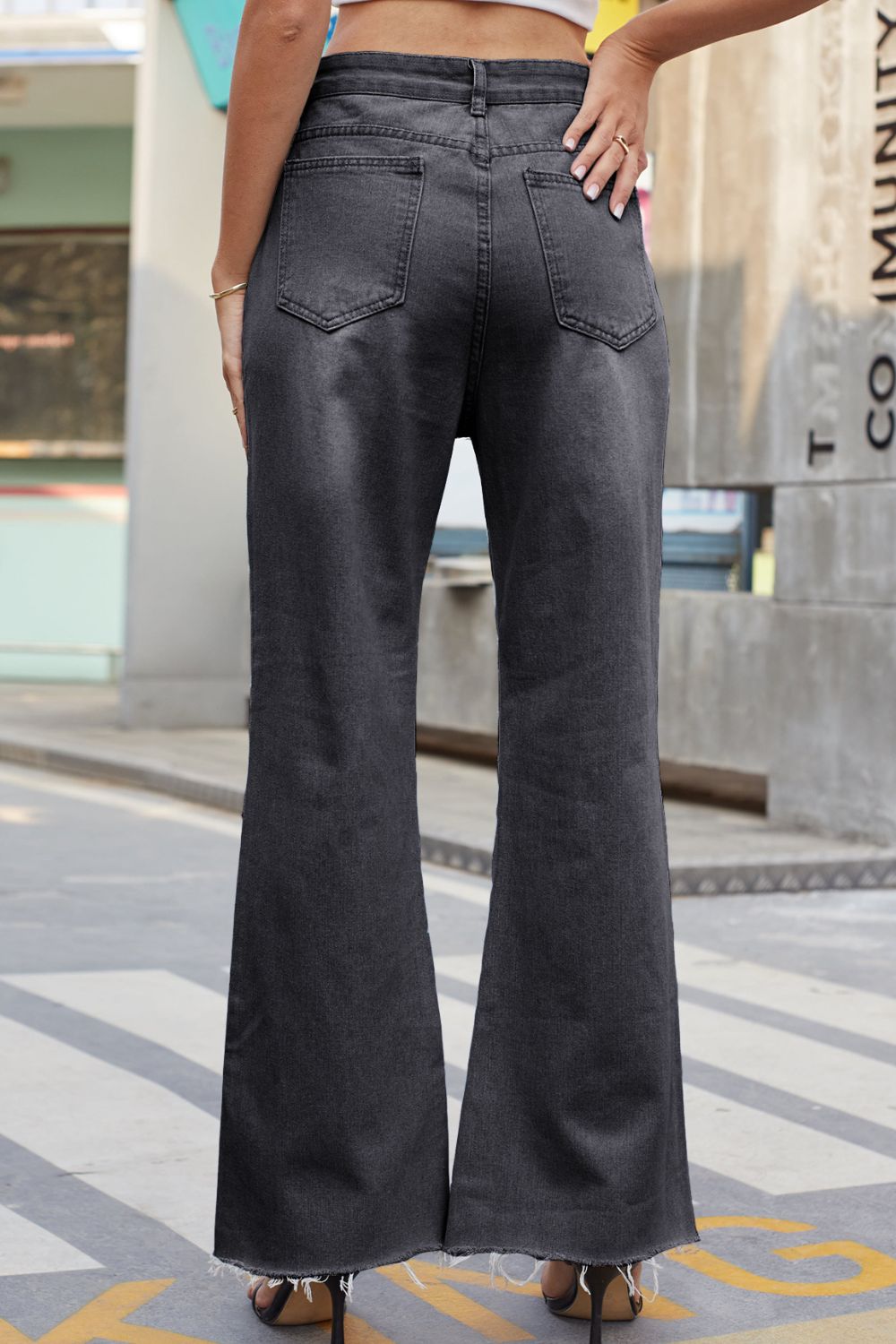 Person wearing black flared jeans standing on a city street.