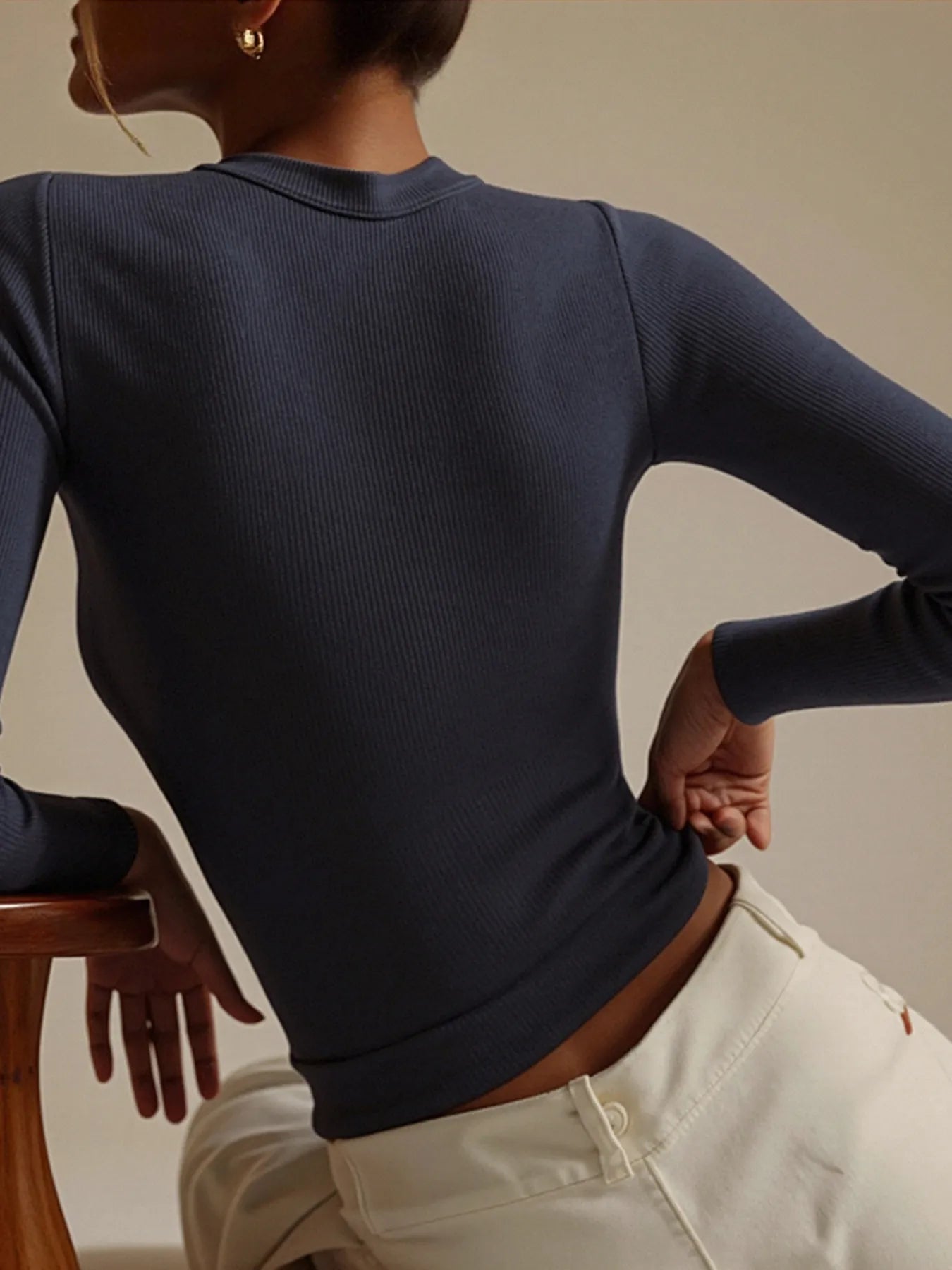 Person wearing a dark blue long-sleeve top and light-colored pants against a neutral background