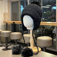 Black knitted hat with pom-poms on a mannequin head in a cafe setting