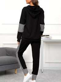 Person wearing a black hoodie and pants with houndstooth pattern on sleeves and legs in a room.