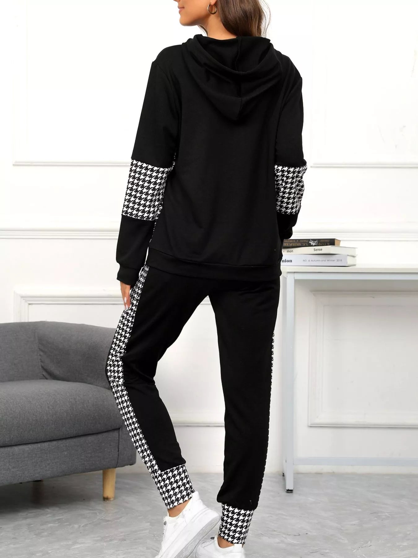 Person wearing a black hoodie and pants with houndstooth pattern on sleeves and legs in a room.