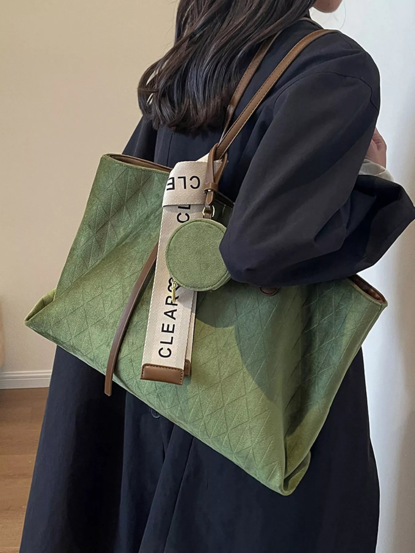 Person holding a green quilted handbag with a visible brand tag.