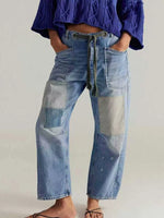 Person wearing blue patchwork jeans with a plain background