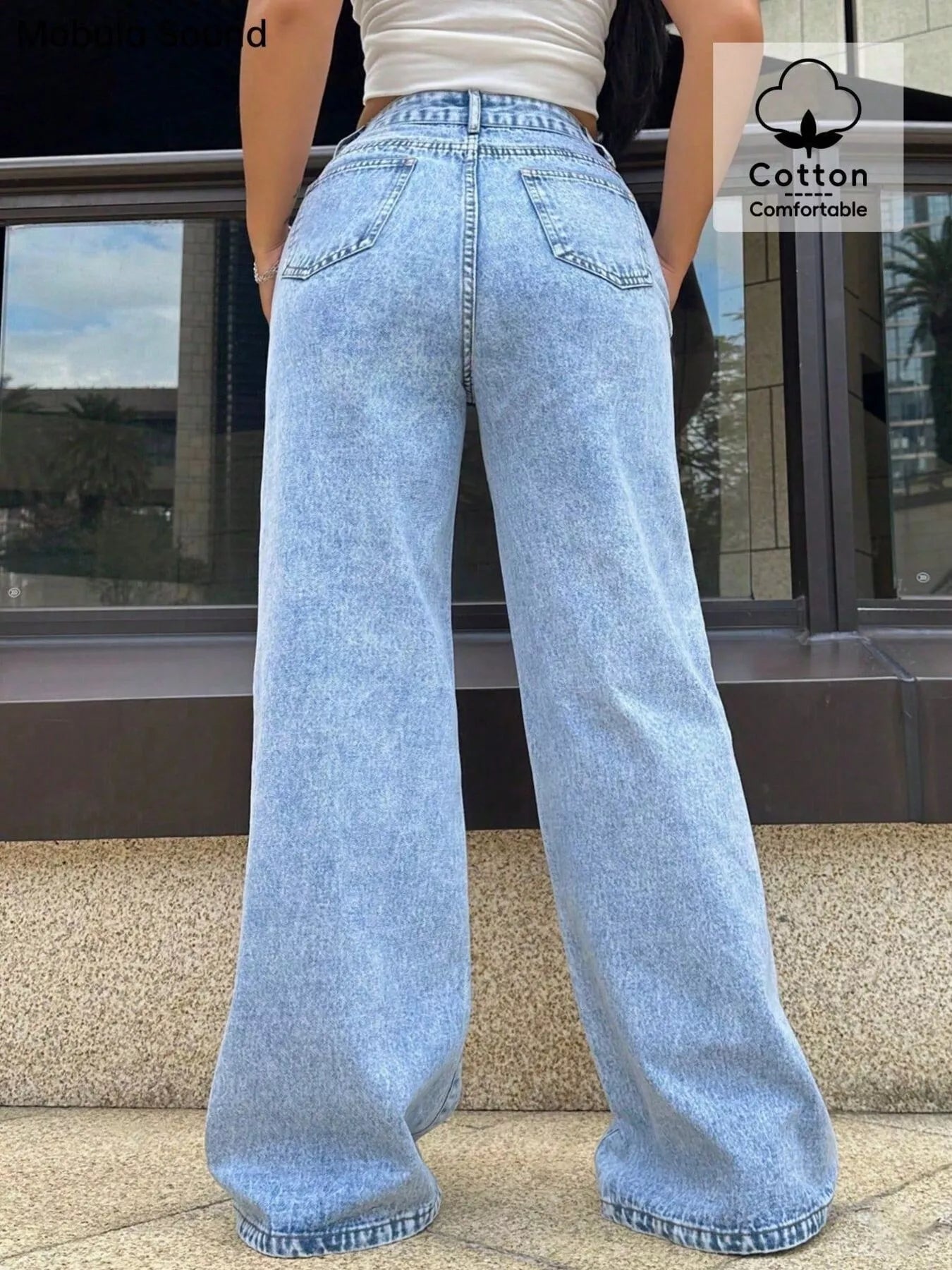 Person wearing light blue jeans with a building in the background