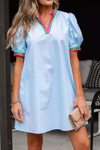 Woman wearing a light blue dress with pink trim, holding a beige clutch.