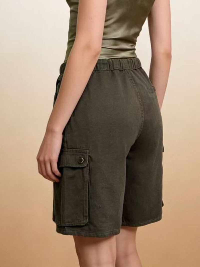 Person wearing olive green cargo shorts on a beige background