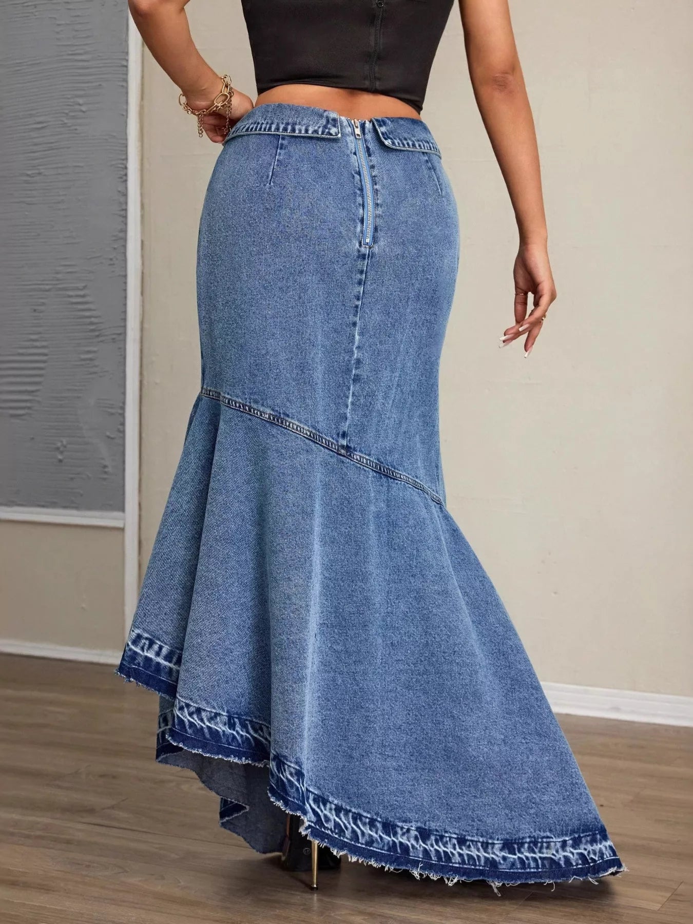 Person wearing a long blue denim skirt with a plain background