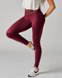 Person wearing maroon leggings and white sneakers on a gray background