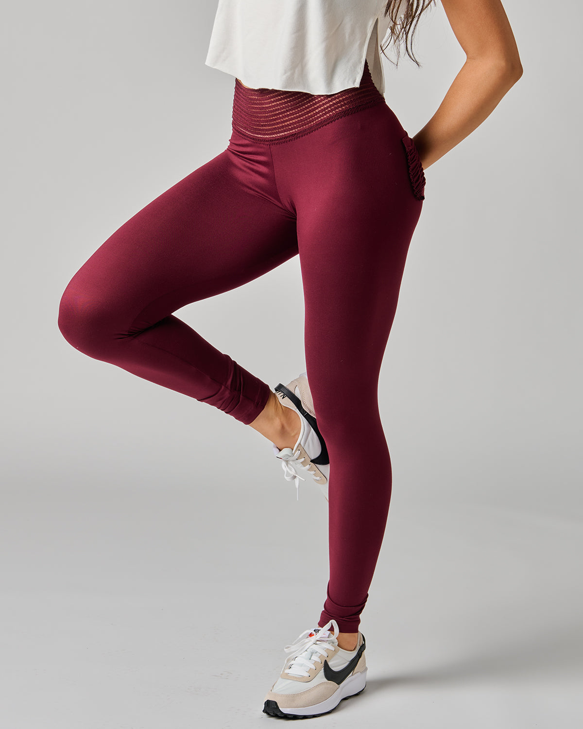 Person wearing maroon leggings and white sneakers on a gray background