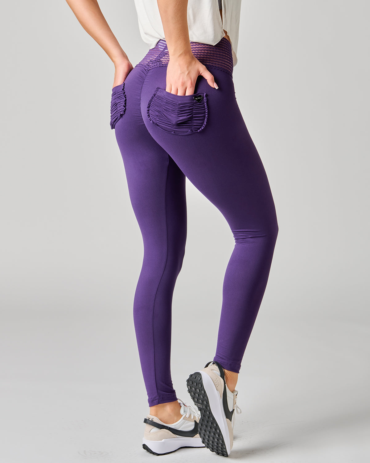 Purple leggings with front pockets worn by a person on a gray background