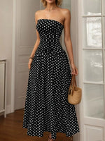 Woman wearing a black strapless dress with white polka dots, holding a woven bag indoors.