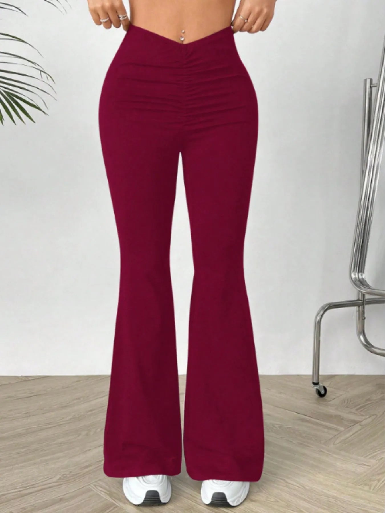 Maroon flared pants worn by a person on a light wooden floor with a white wall background.