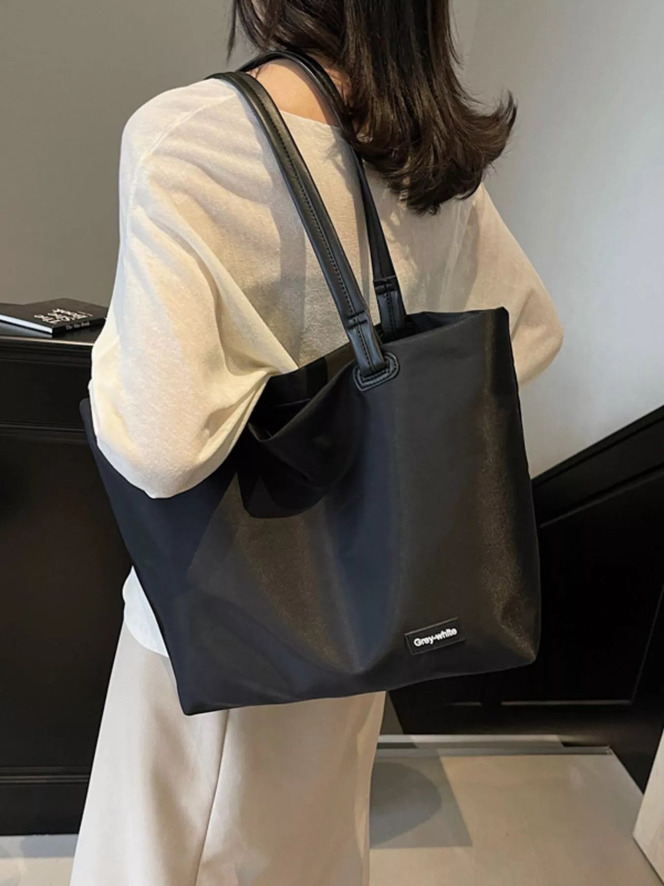 Person holding a black tote bag with a visible brand logo indoors.