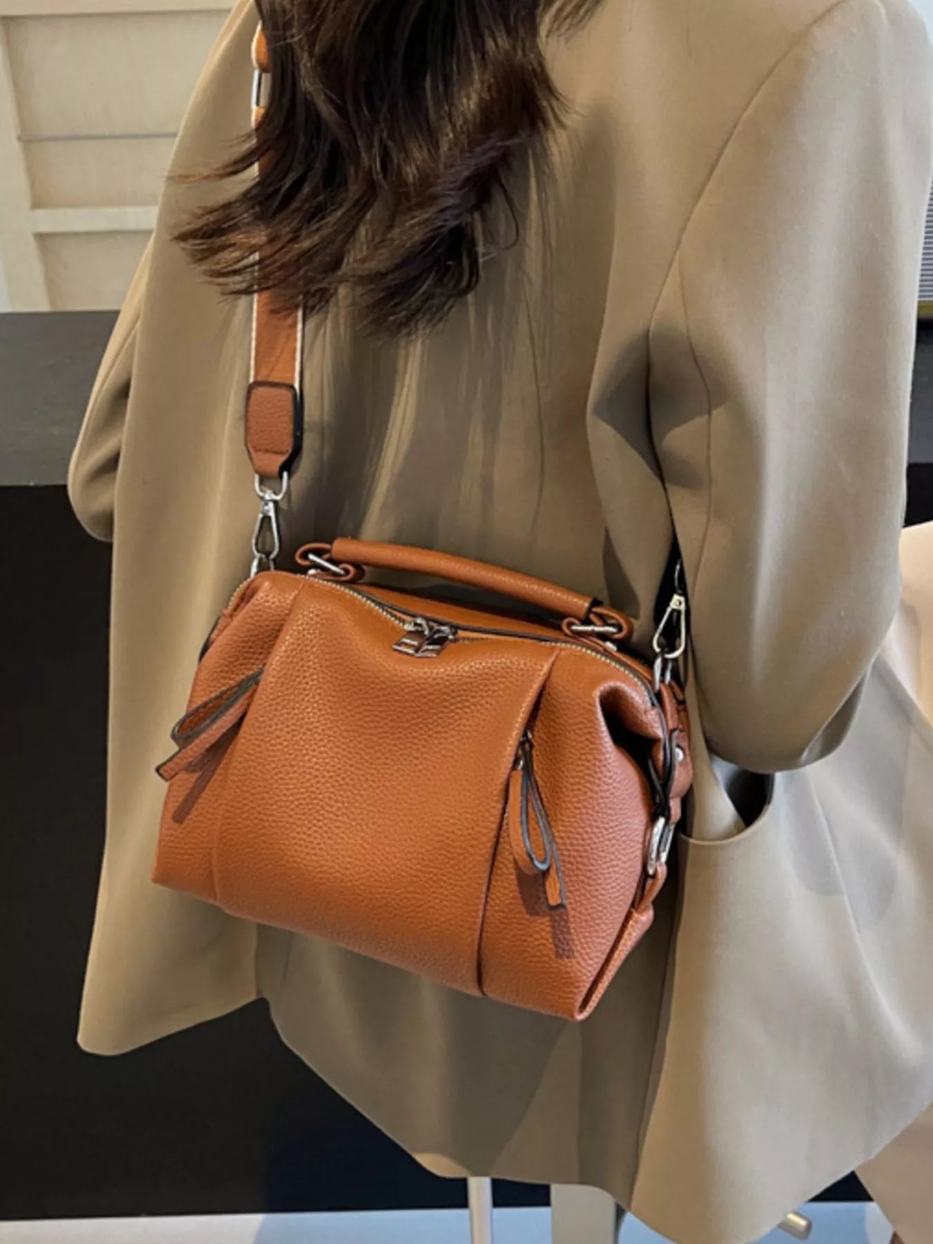 Person wearing a beige coat with a brown leather handbag over the shoulder.