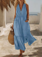 Woman in a blue dress holding a straw bag on a beach.