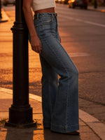 Person wearing blue jeans standing on a sidewalk with a street lamp in the foreground.