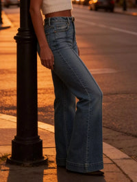 Person wearing blue jeans standing on a sidewalk with a street lamp in the foreground.