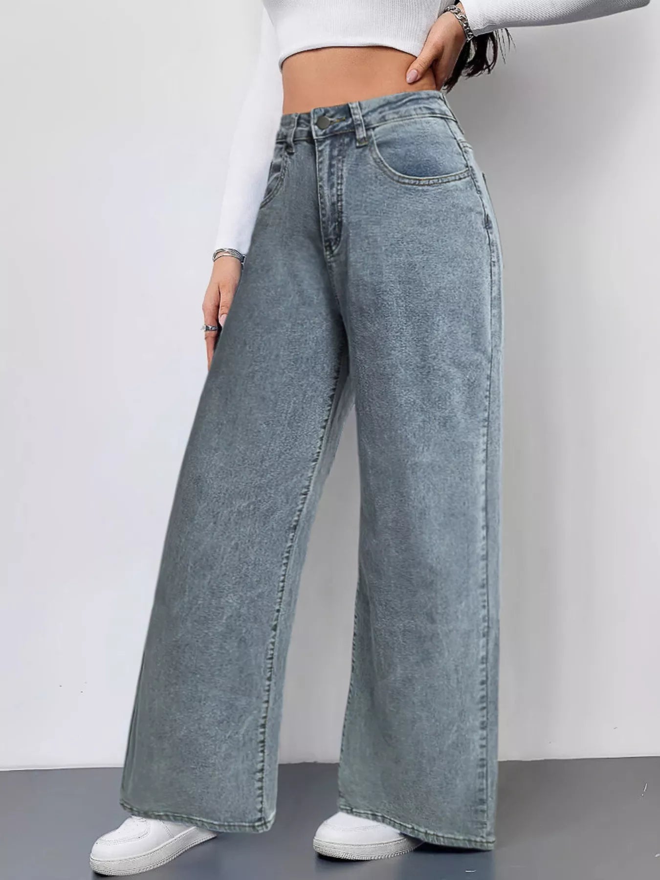 Person wearing wide-leg jeans and a white crop top on a plain background
