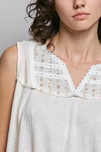 Close-up of a woman wearing a white sleeveless top with lace details.