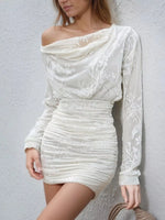A woman wearing a fitted off-the-shoulder mini dress in off-white with tonal floral embroidery, posed against a light textured wall.