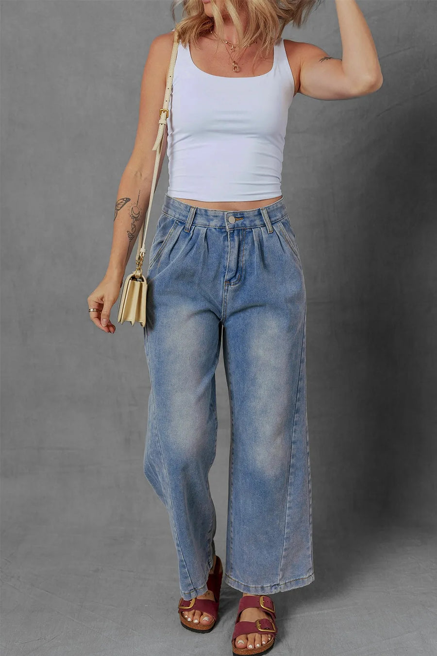 Person wearing a white tank top and blue jeans against a gray background
