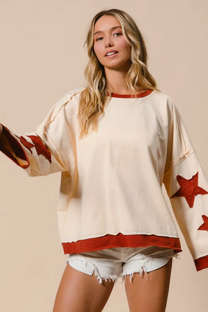Woman wearing a cream-colored top with red accents and star patterns, paired with denim shorts on a beige background.