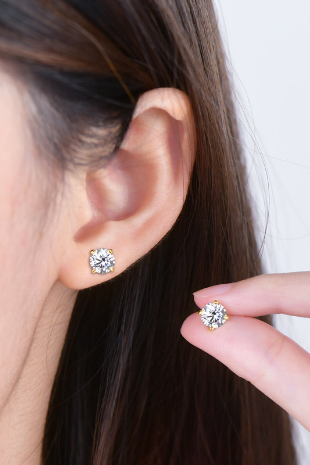 Close-up of an ear wearing a diamond earring with another earring held in hand.