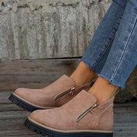 Beige ankle boots with zippers worn with blue jeans on a wooden floor.