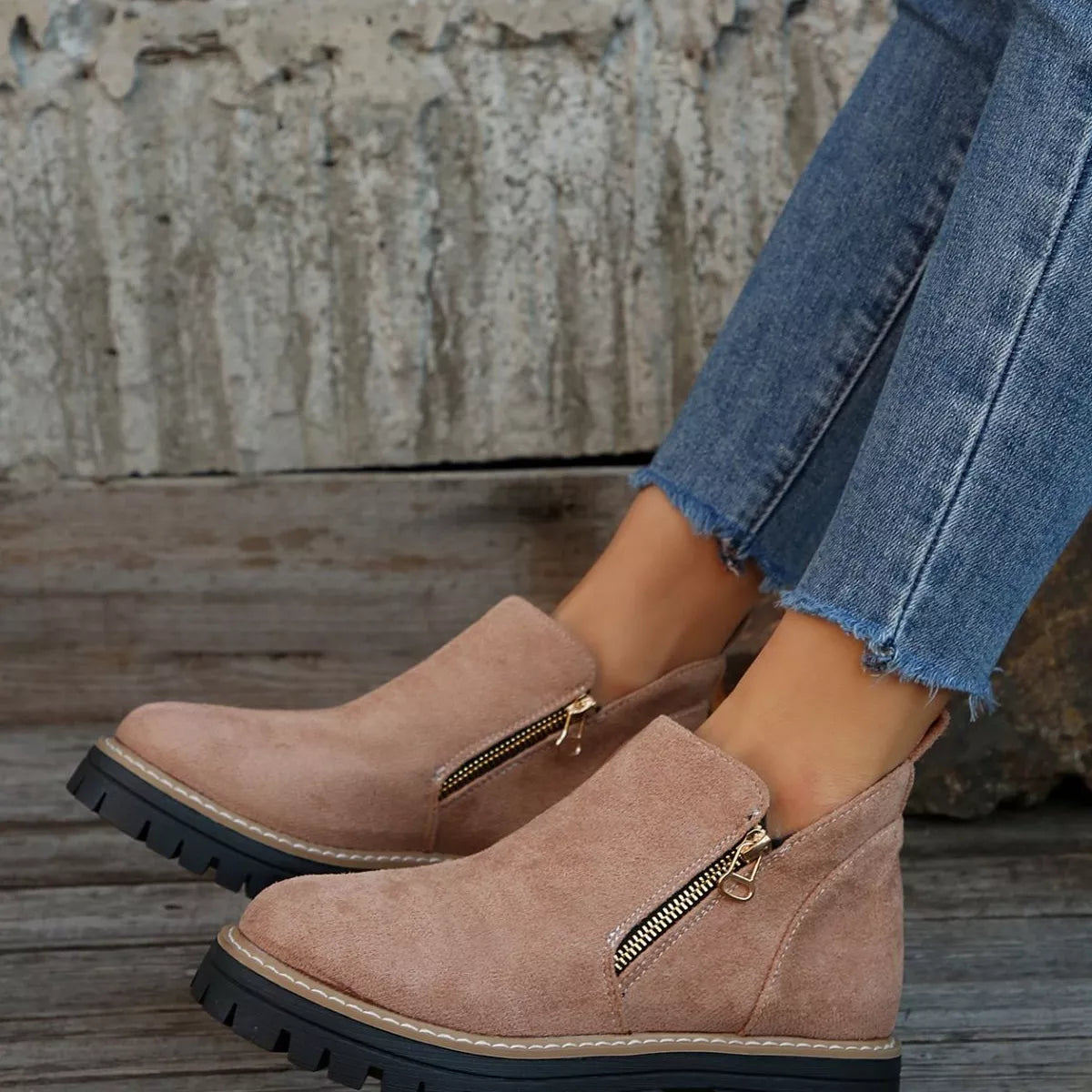 Beige ankle boots with zippers worn with blue jeans on a wooden floor.