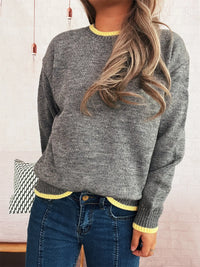 Person wearing a gray sweater with yellow trim and blue jeans indoors.