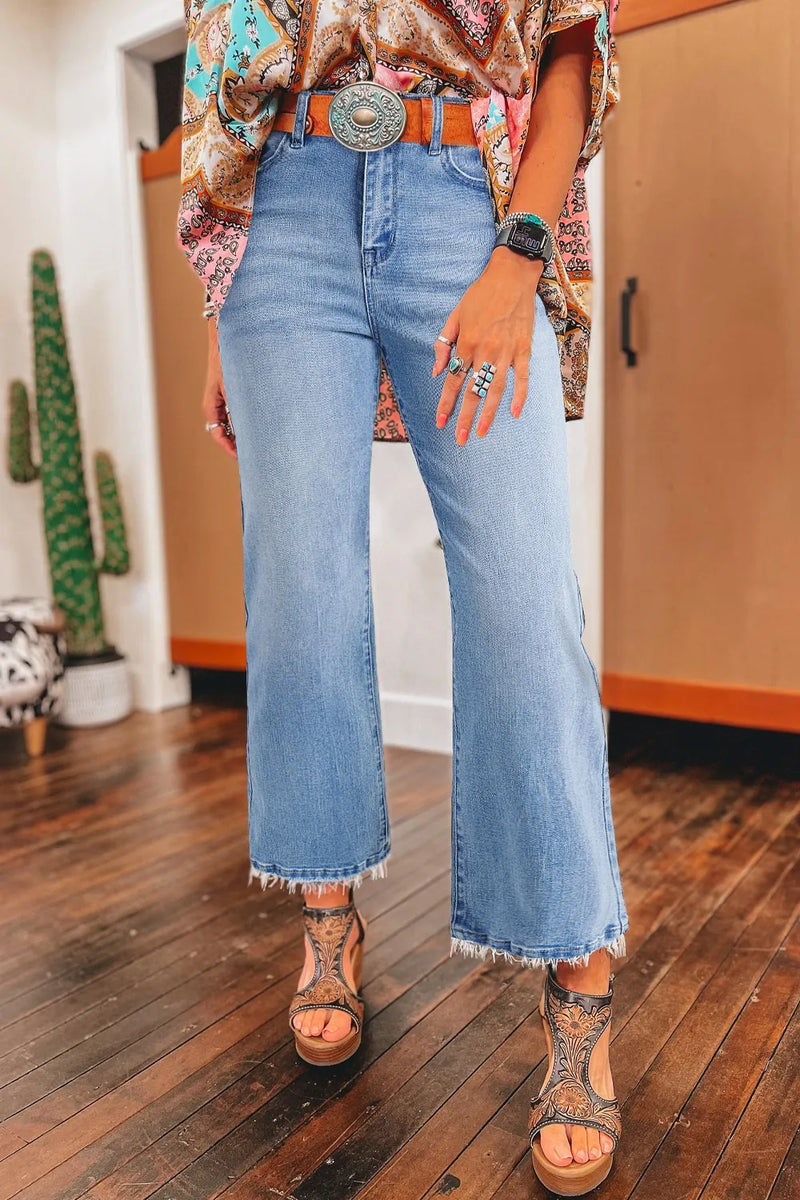Person wearing blue jeans and a patterned top with a belt, standing on a wooden floor.