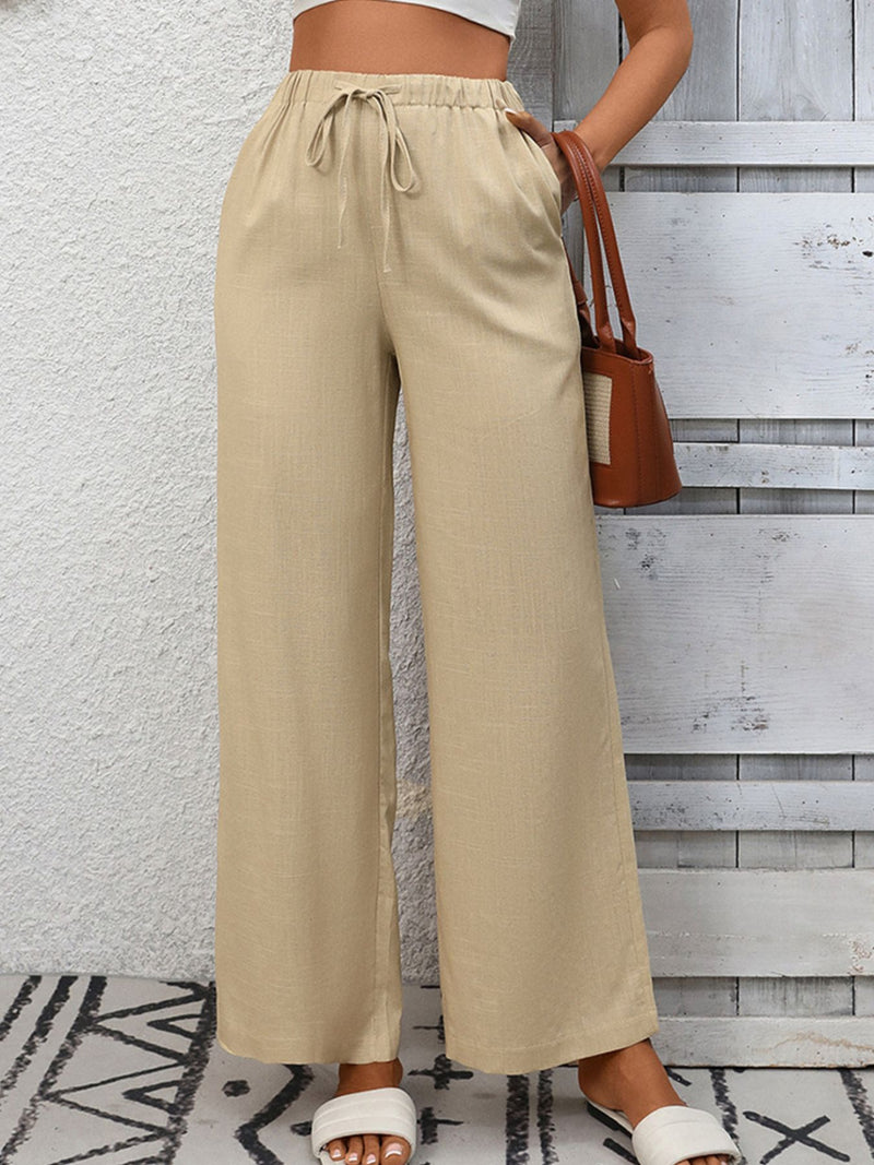 Person wearing beige wide-leg pants with a white wall and wooden floor background