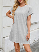 Woman wearing a gray patterned dress standing against a light-colored wall.