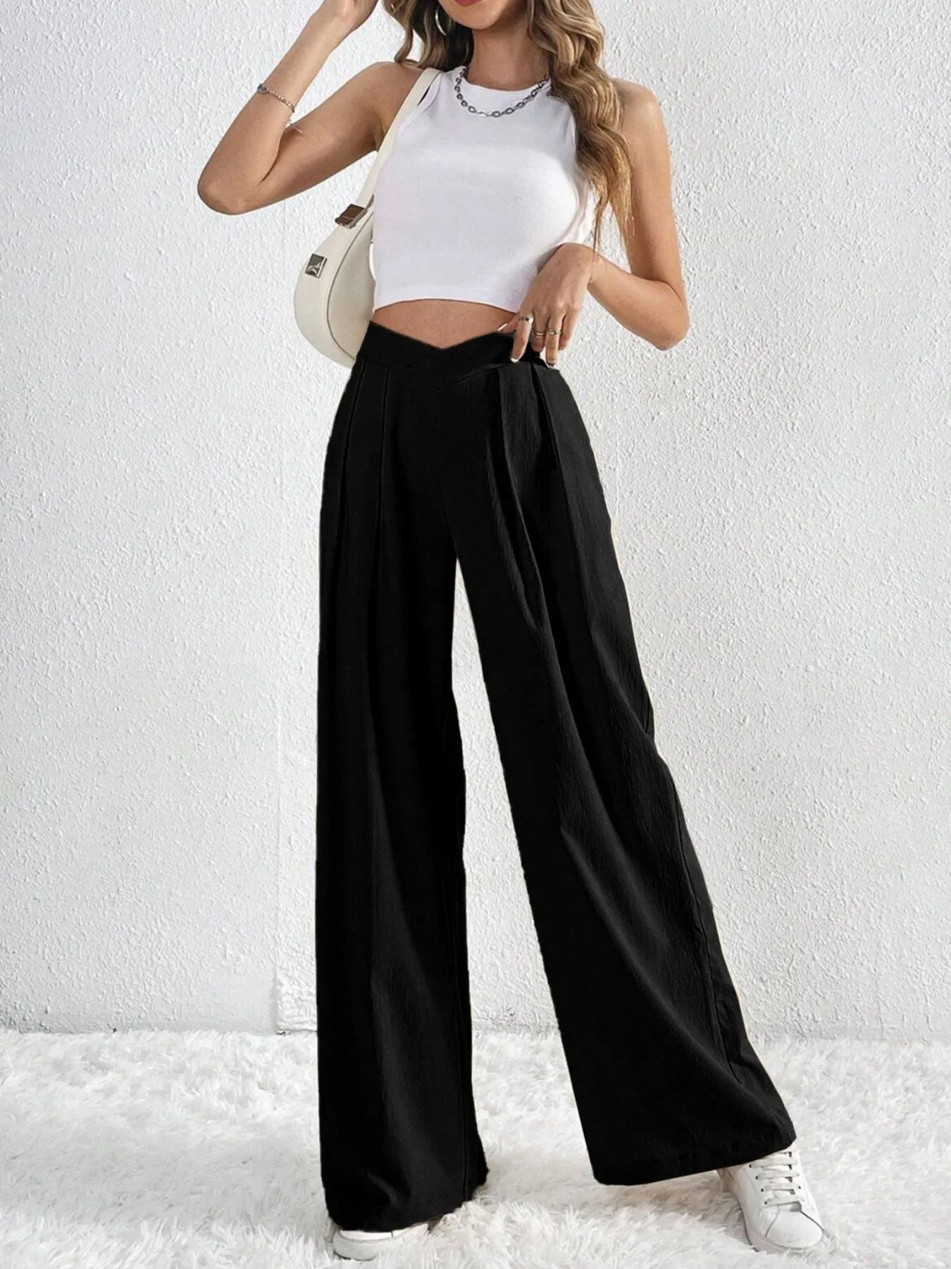 Person wearing a white crop top and black wide-leg pants against a white background