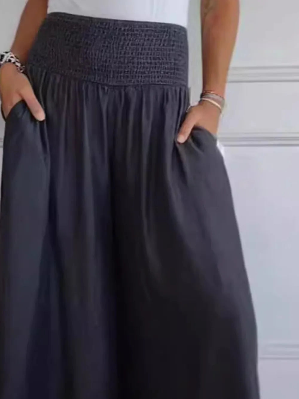 Person wearing a dark gray skirt with hands in pockets against a light background
