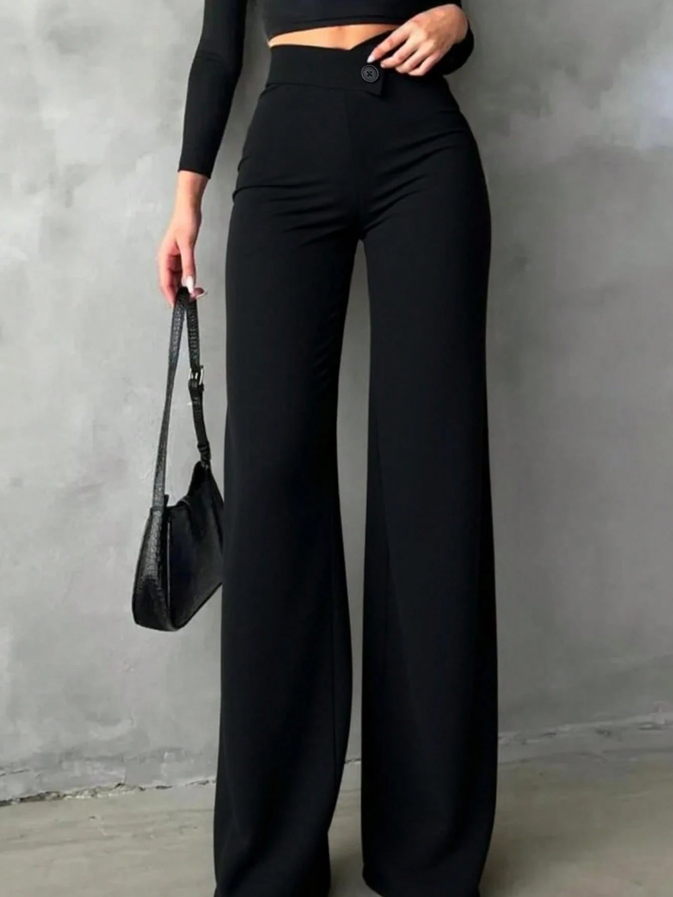 Person wearing black high-waisted pants and a black top against a gray wall.