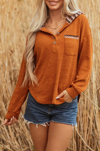 Woman wearing an orange long-sleeve shirt and denim shorts standing in a field of tall grass.