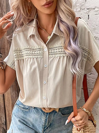 Woman wearing a beige button-up shirt with lace details and blue jeans, standing against a textured wall.