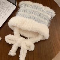 Fluffy white and gray knitted hat on a wooden surface with a laptop.
