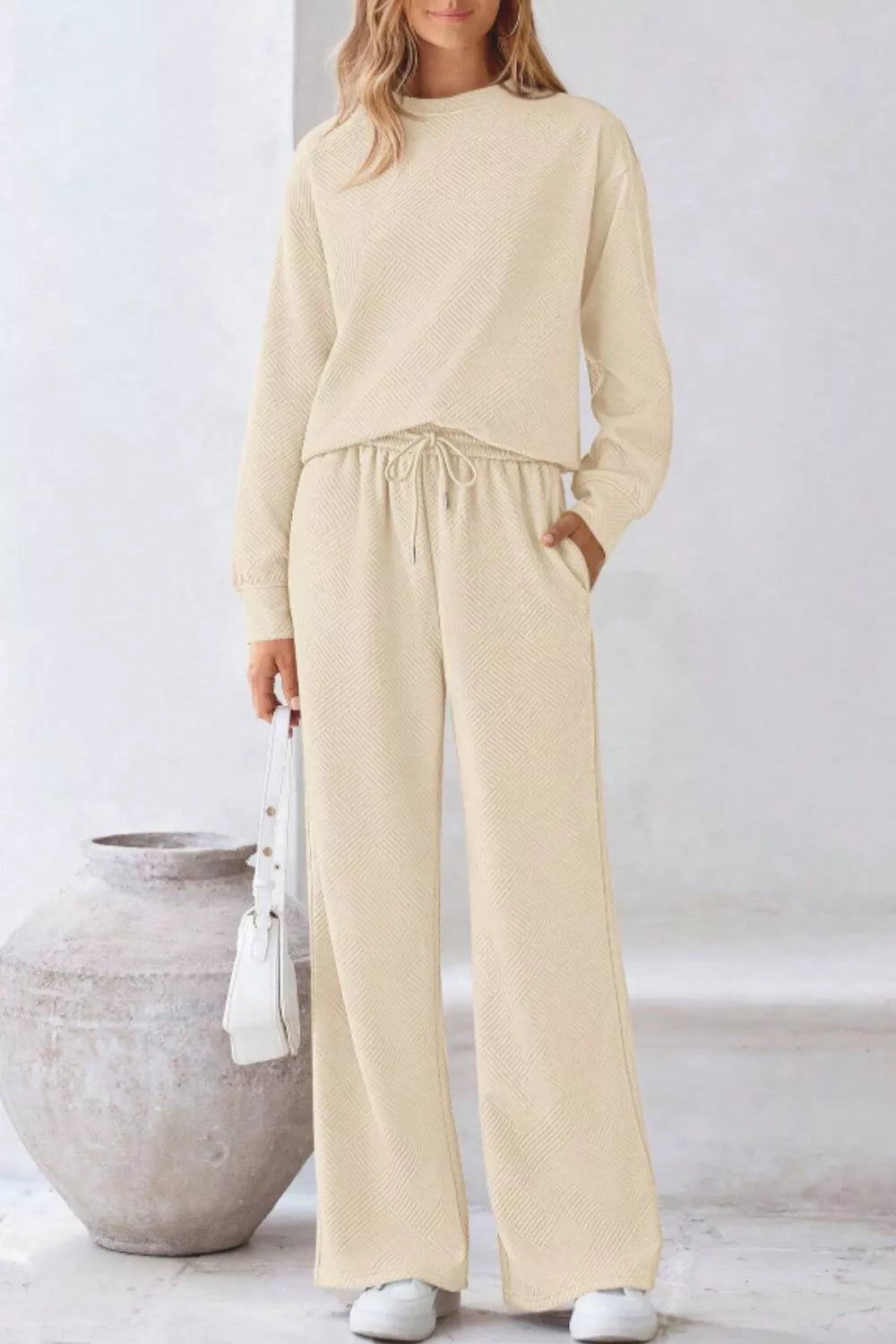 Person wearing a beige outfit standing next to a large pot indoors.