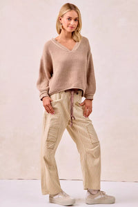 Woman wearing a beige sweater and striped pants against a plain background
