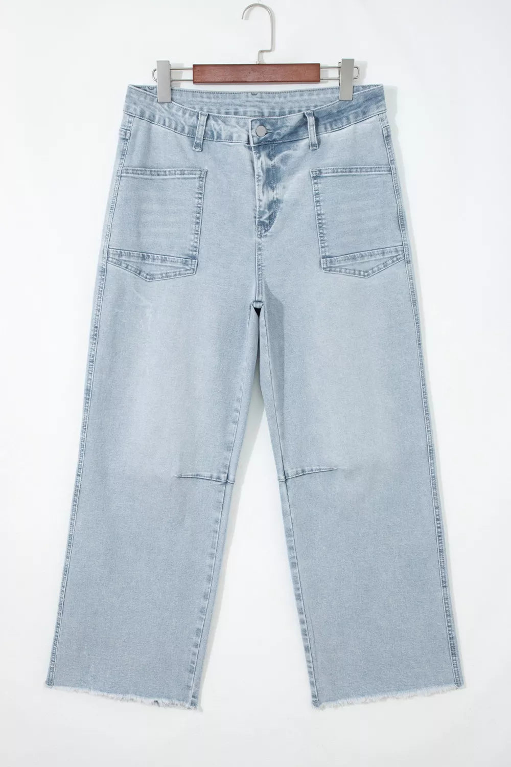 Light blue jeans hanging on a wooden hanger against a white background