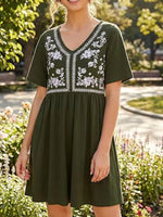 Woman wearing a green dress with white embroidery in a garden setting