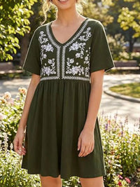 Woman wearing a green dress with white embroidery in a garden setting
